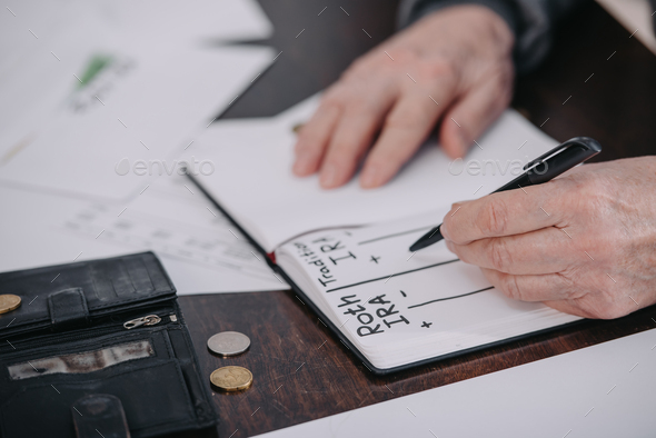 cropped view of senior woman writing in notebook with roth ira and traditional ira words - Stock Photo - Images
