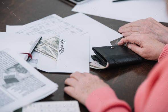 cropped view of senior couple sitting at table with paperwork, money and envelope with 'roth ira' - Stock Photo - Images