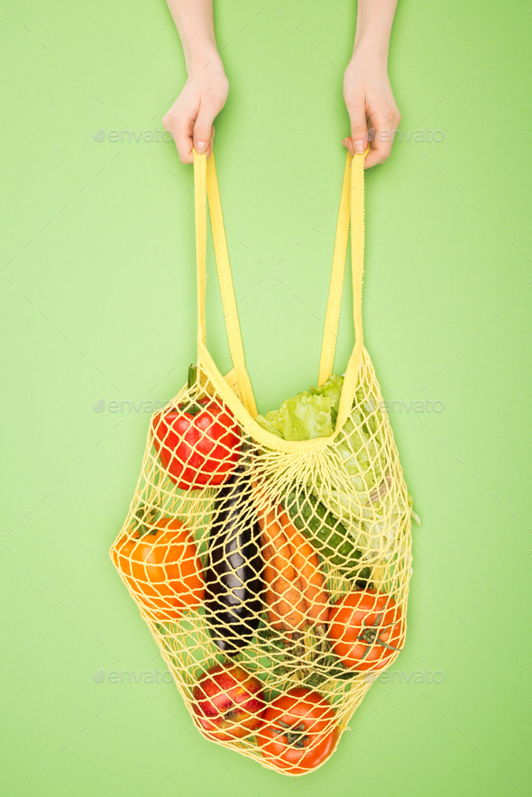 cropped view of woman holding string bag with vegetables on light green
