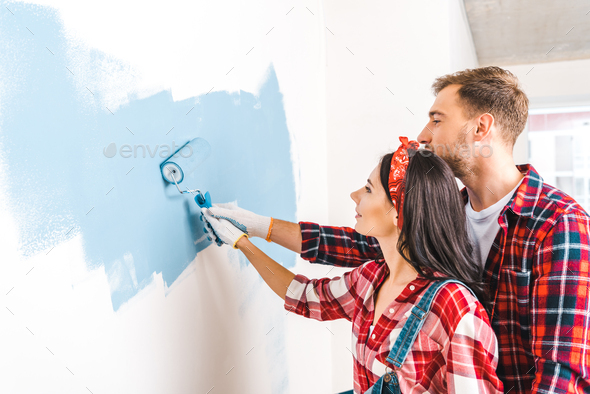 cheerful man and woman painting wall in blue color at home