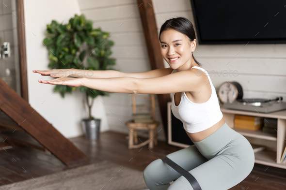 Cute Asian Fitness Girl At Home Doing Workout Squats With Stretching Elastic Rope On Her Legs