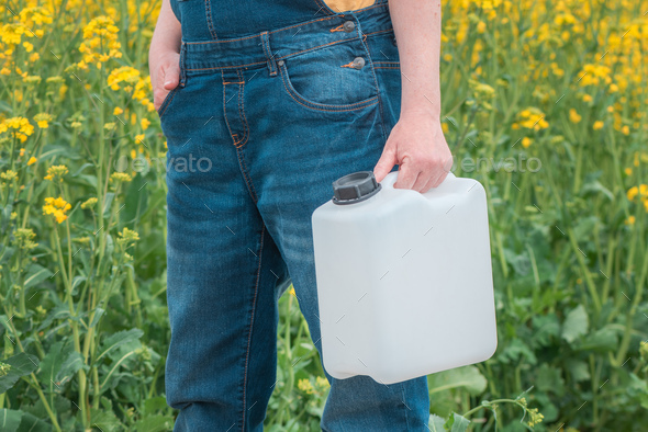 Rapeseed crop protection concept, female farmer agronomist holding jerry can bottle with pesticide