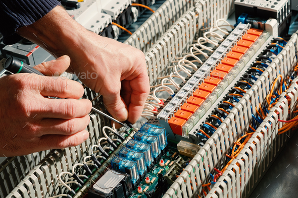 Electrical installation works. Worker\'s hands on the background of the circuit board.