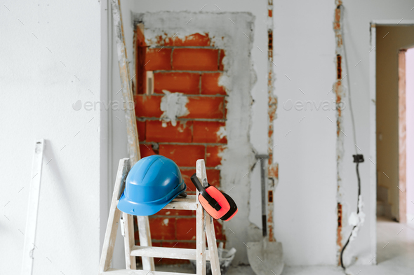 ladder, blue protective helmet and ear defenders at construction site. Home improvement. Bricks wall