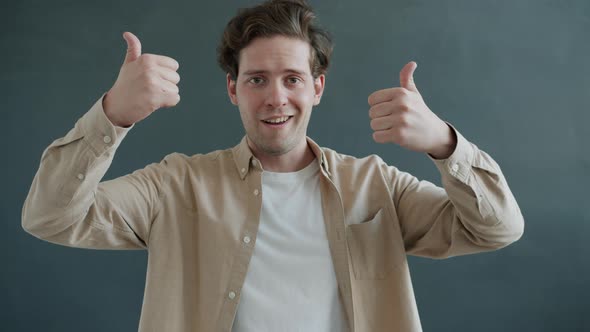 Portrait of Young Man Showing Thumbsup Then Thumbsdown Hand Gesture and Looking at Camera with alt