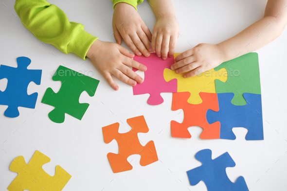 Close-up of children\'s small hands connecting puzzle pieces.
