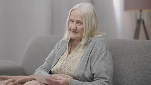 Sad Hopeless Old Woman Caressing Picture in Hands Looking at Camera Sighing alt