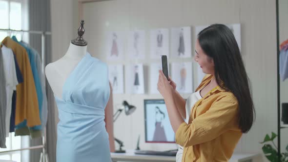 Female Designer Using Smartphone Taking Photo Of A Dress On A Mannequin While Designing Clothes alt
