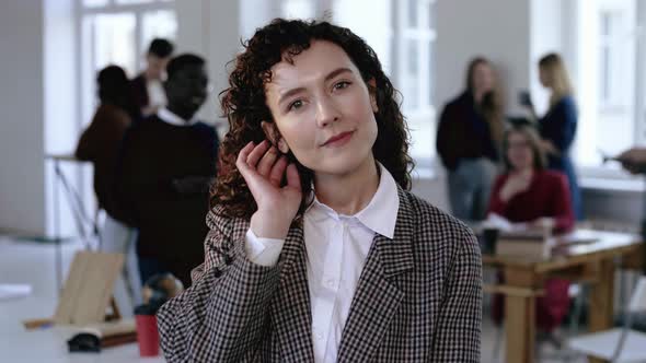 Young Serious European Business Woman in Formal Suit Touching Her Dark Curly Hair Posing at Modern alt