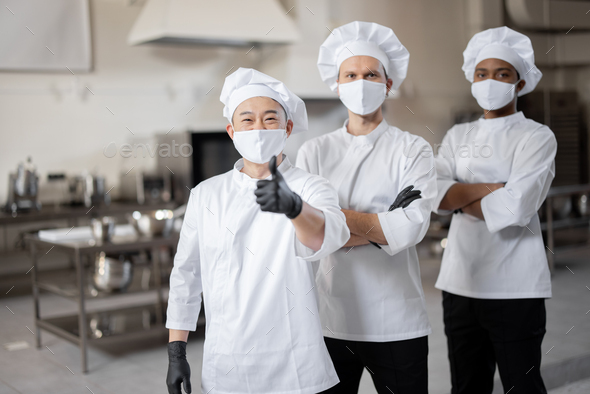 Three well-dressed chefs standing together in the professional kitchen ...