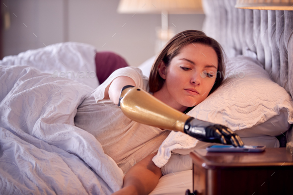 Couple With Woman With Prosthetic Arm Sleeping In Bed Before Being Woken By Mobile Phone Alarm