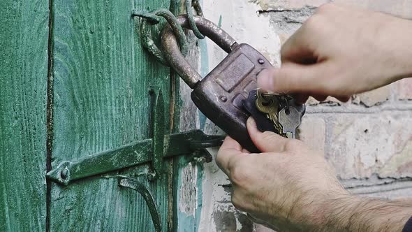 Closeup of a Caucasian Man's Hand Opens Old Padlock That is Hanging
