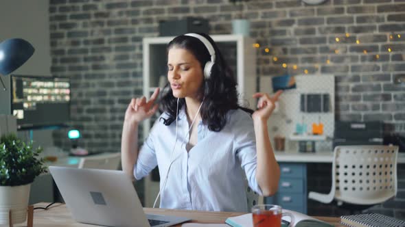 Playful Girl Dancing Enjoying Music in Headphones and Using Laptop in Office alt