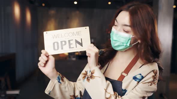 Business owner attractive young asian woman in apron hanging we're open sign. alt