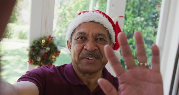 Portrait of happy senior man in santa hat waving hand during christmas video call alt