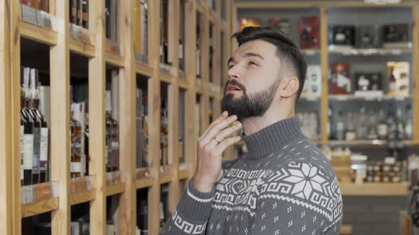 Handsome Bearded Man Looking at the Shelves with Bottles at Wine Store