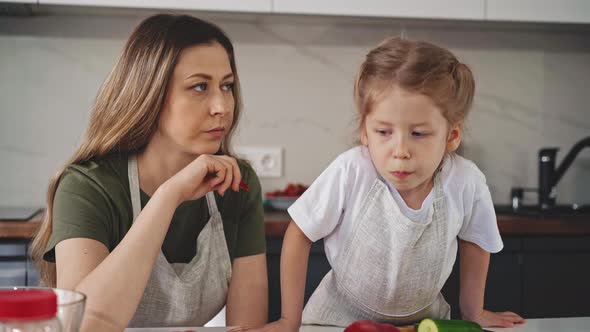 Mother and Daughter Eat Red Bell Pepper at Table in Kitchen alt