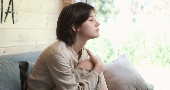 Sad Young Woman Sitting on the Couch and Hugging Herself