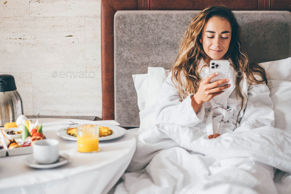 Woman eating breakfast and using phone in the hotel room.