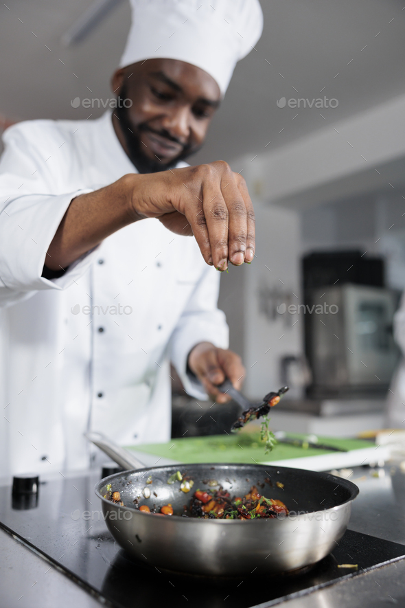Head cook throwing fresh chopped herbs in pan to improve taste of meal while in professional kitchen