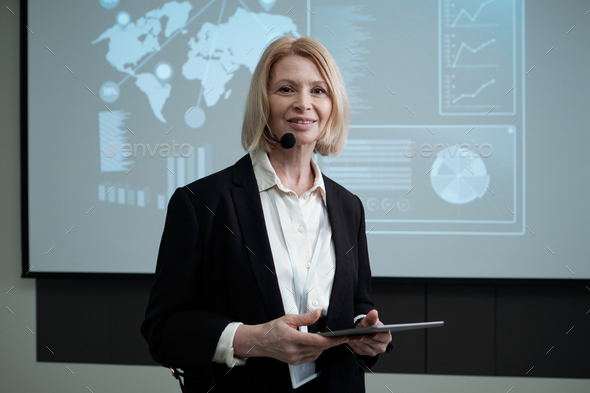 Happy mature female broker with tablet looking at camera against board