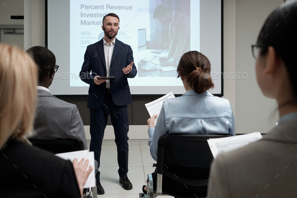 Young confident broker in elegant suit making presentation by interactive board