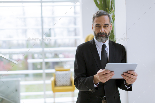 Handsome mature businessman with tablet in the office working, reading or searching something
