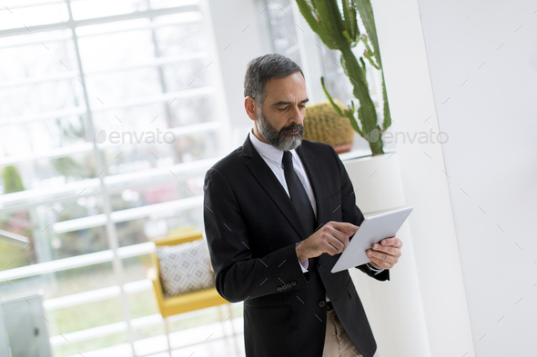 Handsome mature businessman with tablet in the office working, reading or searching something