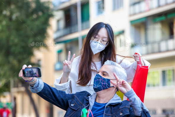 Cheerful friends in masks taking selfie in city