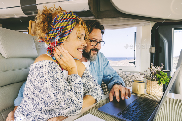 Adult man and woman using together a laptop inside a modern camper van. Couple in van life