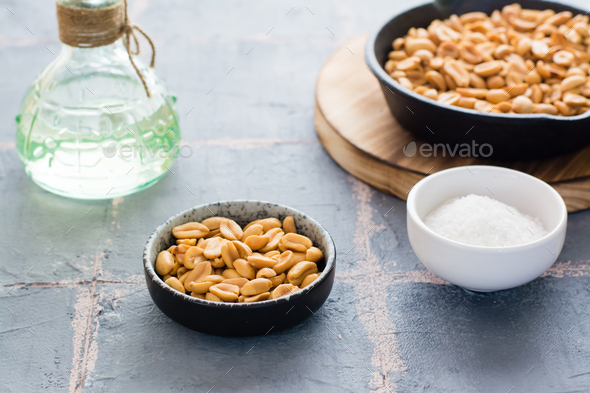 Roasted peanuts in a bowl and in a frying pan, a bowl with salt on the table.