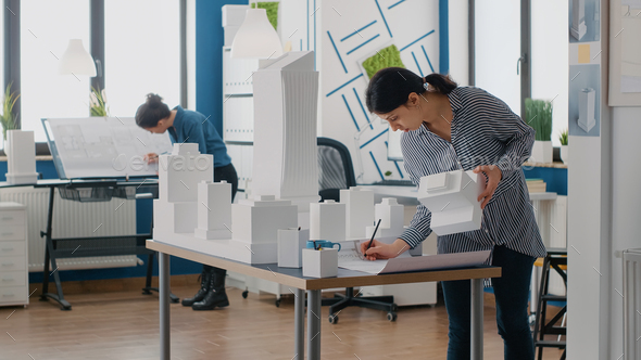 Contractor holding building model to design blueprints plan on table