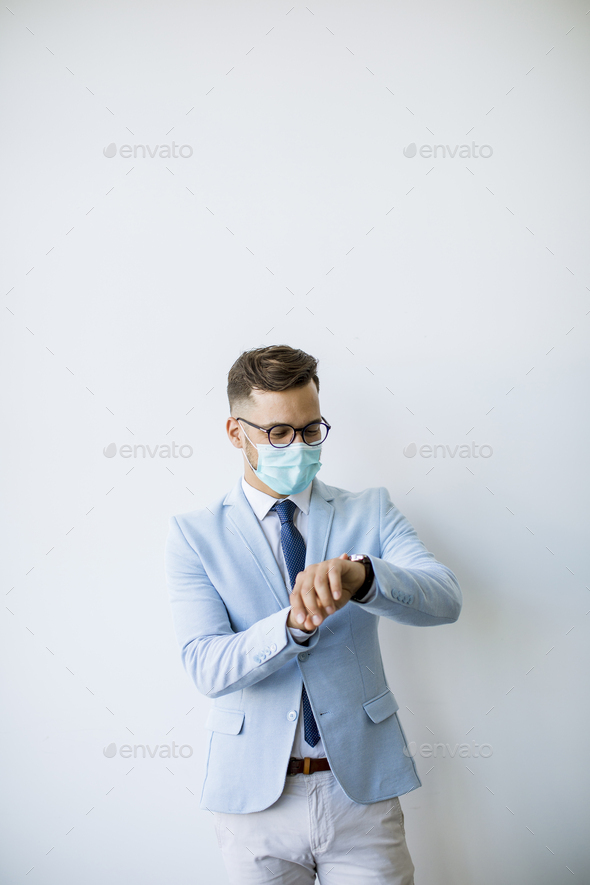 Young and stylish business man with face mask stands by the wall in the