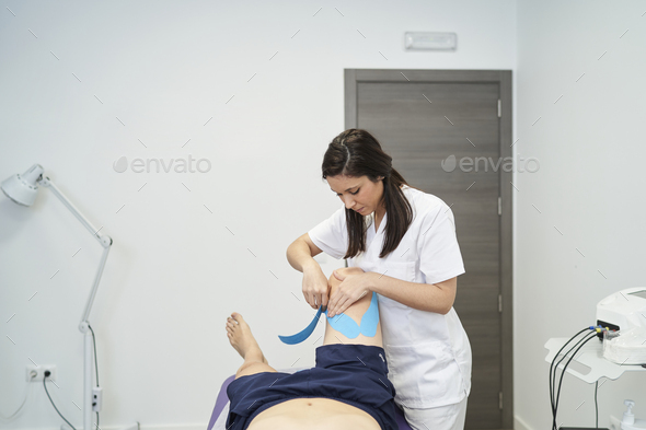 physiotherapist treating the patient\'s knee with neuromuscular taping