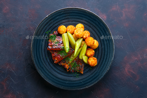 Top view of grilled ribs with pickled cucumber and fried potato balls