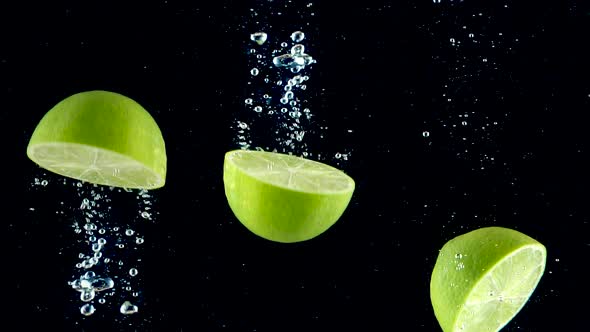 Limes splashing into the water in slow motion. Three half of limes falling slowly