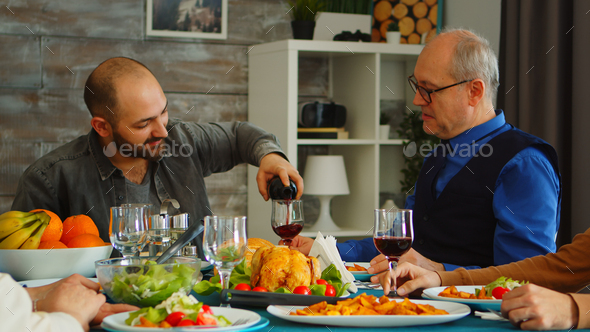 Young man serving his father in law with red wine