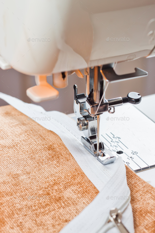 Modern sewing machine sews on the zipper on beige item of clothing