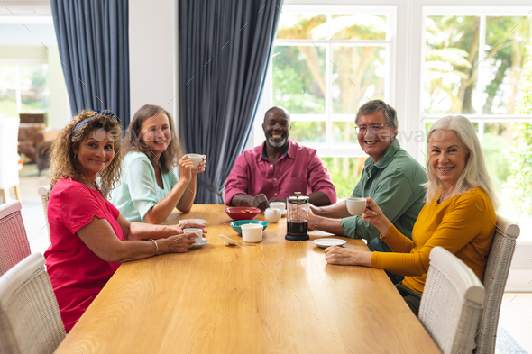 Portrait of smiling multiracial senior female and male friends having coffee together at home