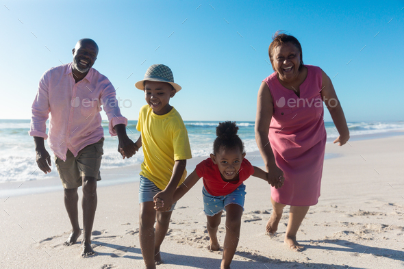 African american grandparents and grandchildren enjoying sunny day together at beach