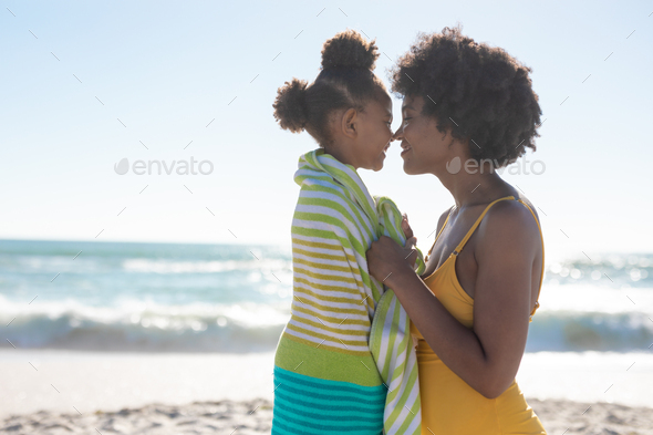 Side view of african american mother and daughter rubbing noses at beach on sunny day