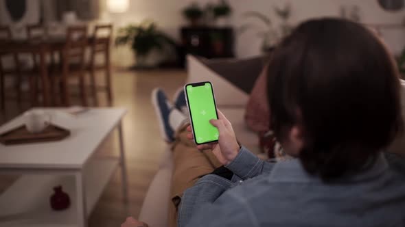Home Isolated. Man at Home Lying on a Sofa Using Smartphone with Green Screen, Doing Swiping