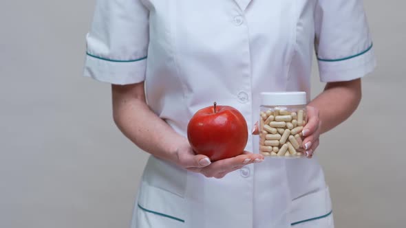 Nutritionist Doctor Healthy Lifestyle Concept - Holding Organic Red Apple and Jar of Vitamin Pills alt
