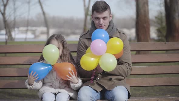 Positive Young Man and Little Girl Moving Down Colorful Balloons and Smiling at Camera. Cheerful alt