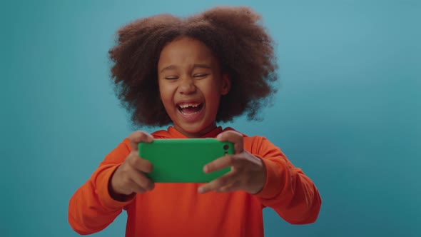 Cheerful African American girl playing video game using mobile phone game application alt