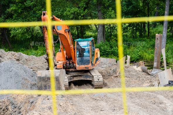 Excavator performs excavation work on the construction site. Yellow tractor digs the ground