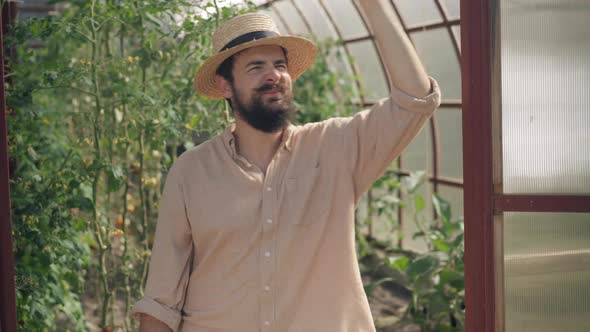 Thoughtful Handsome Male Farmer Standing in Greenhouse Leaning on Door Smiling alt