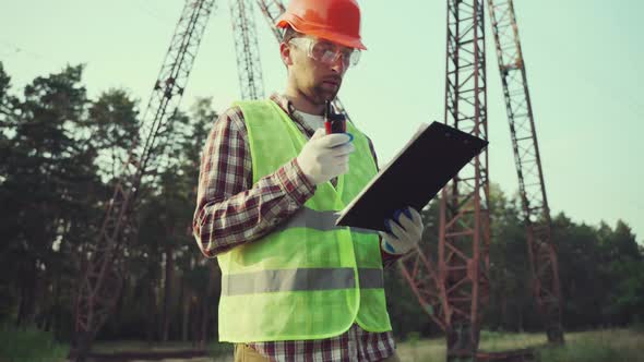 Electrical Engineer Wearing Hard Hat and Safety Vest Checking Electrical Systems on High Voltage alt