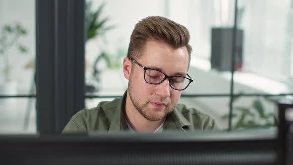 Male Office Worker Talking on Phone Young Man with Glasses Communicates on Smartphone While Working alt