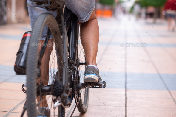 Close up on casual woman\'s legs while running her electro bicycle in urban street